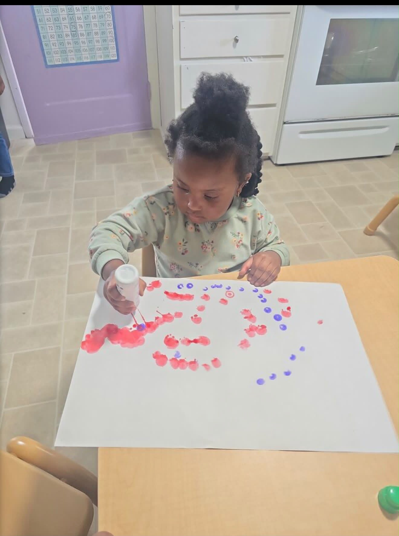 Child painting with red and purple dot markers